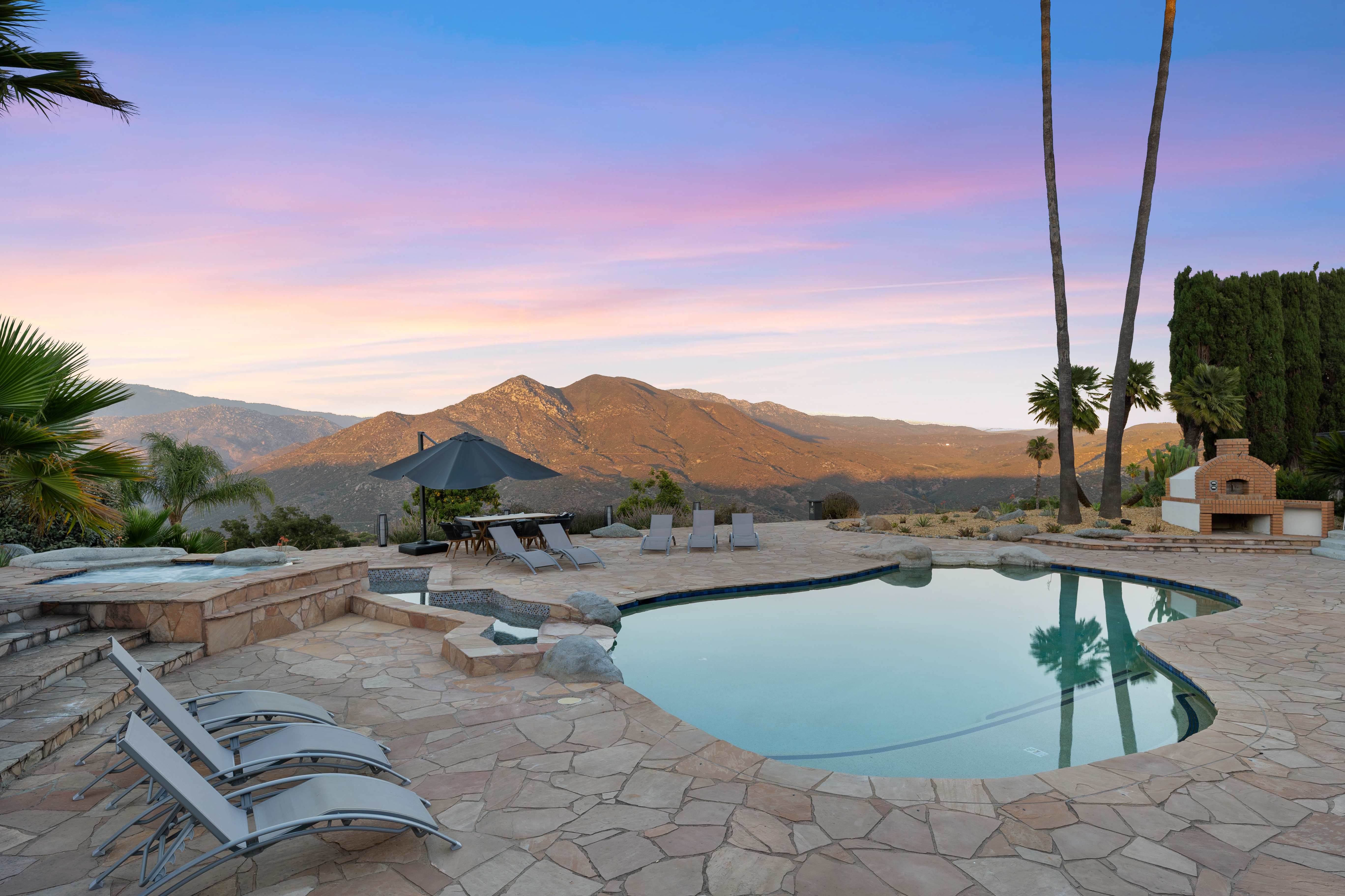 Pool area at sunset with hot tub, lounge chairs, and mountain panorama