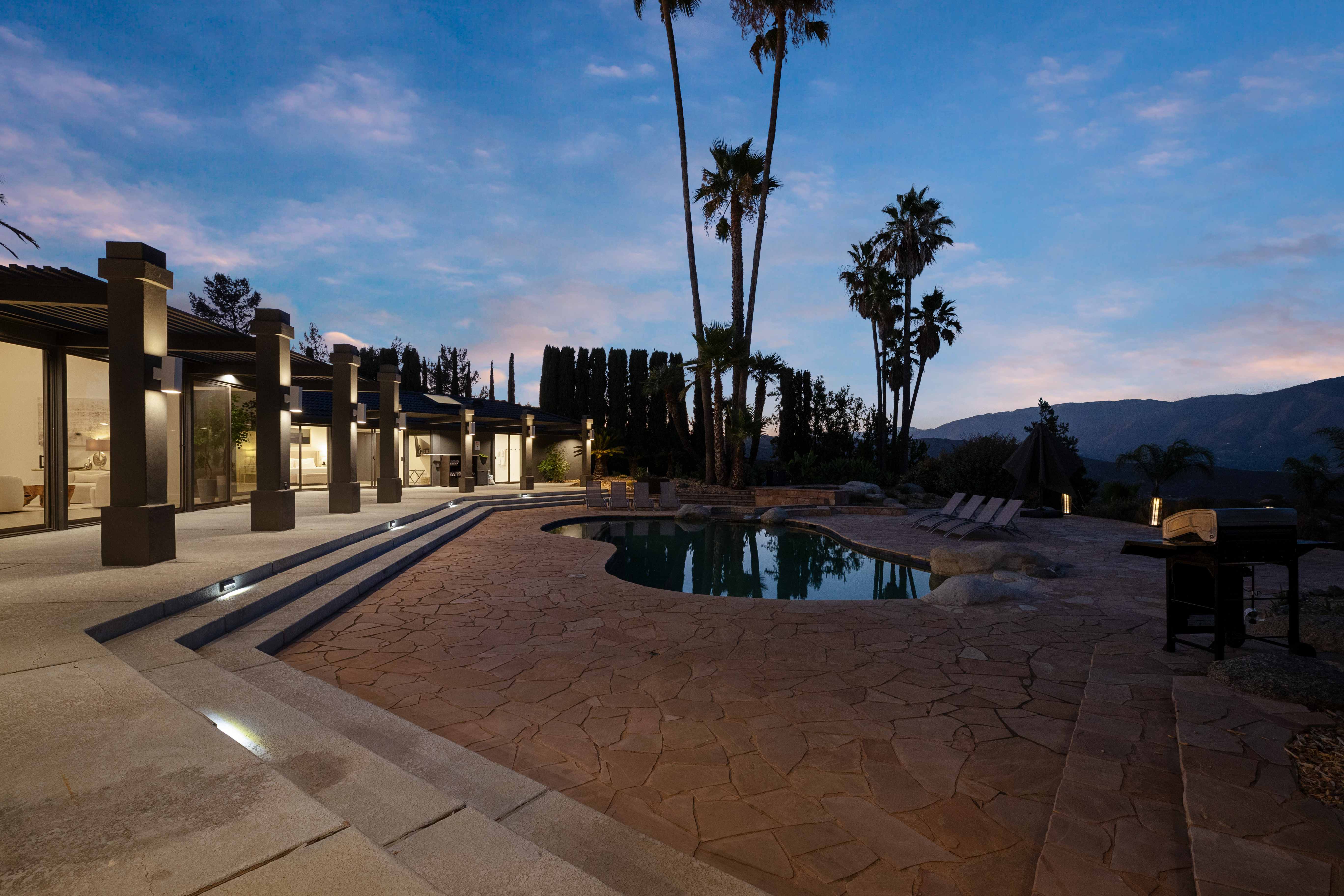 Evening exterior with lit columns, pool, and step lighting