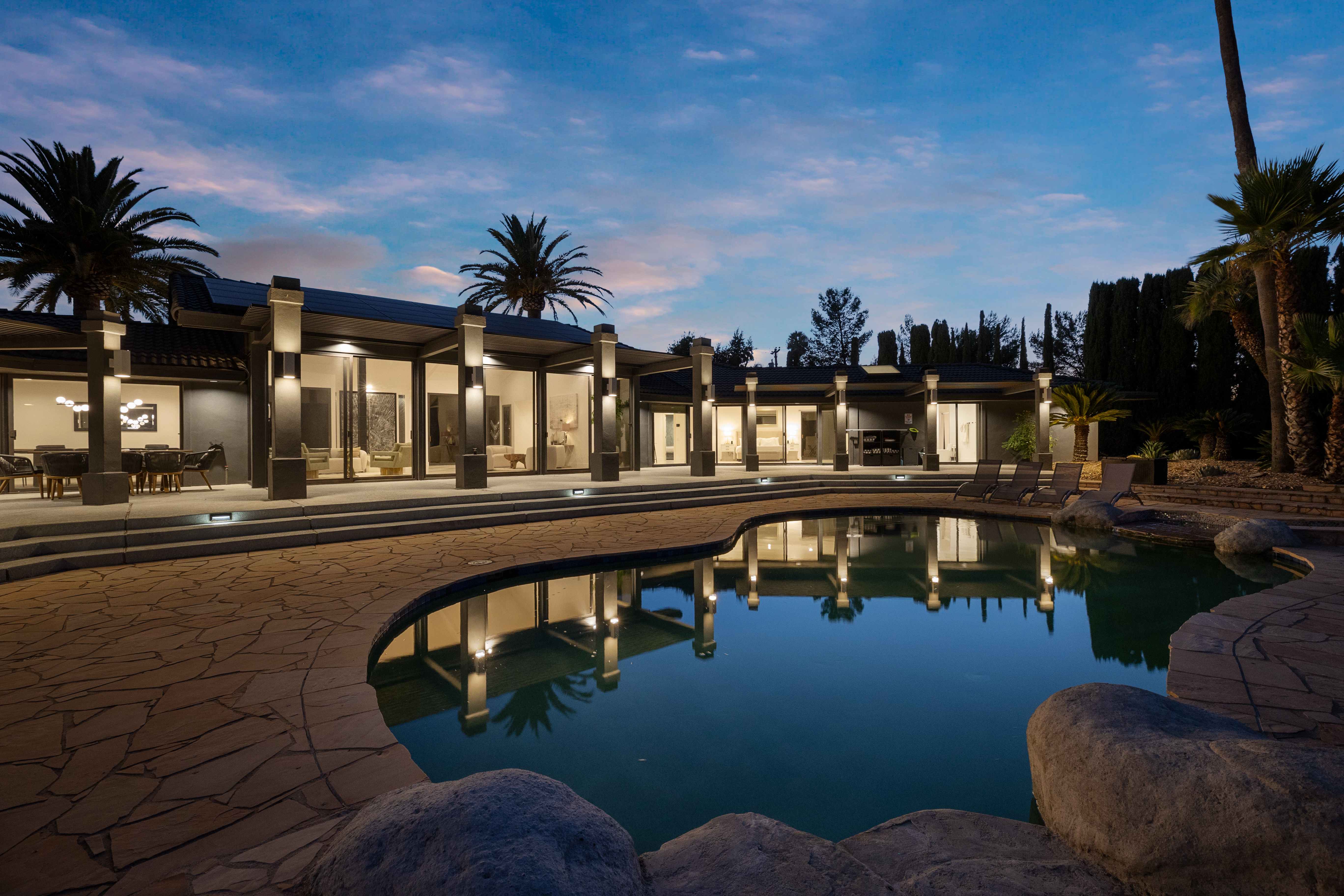 Evening view of house from pool with illuminated columns reflecting in water